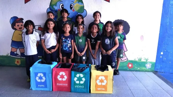 Estudantes uniformizados ao lado de lixeiras temáticas de coleta seletiva e reciclagem