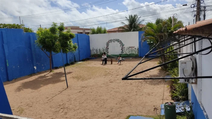 Área do pátio com canteiro arborizado, árvores frondosas e brinquedo de gangorra